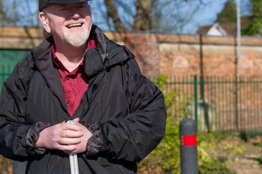 A smiling man holding a cane in the sunshine.